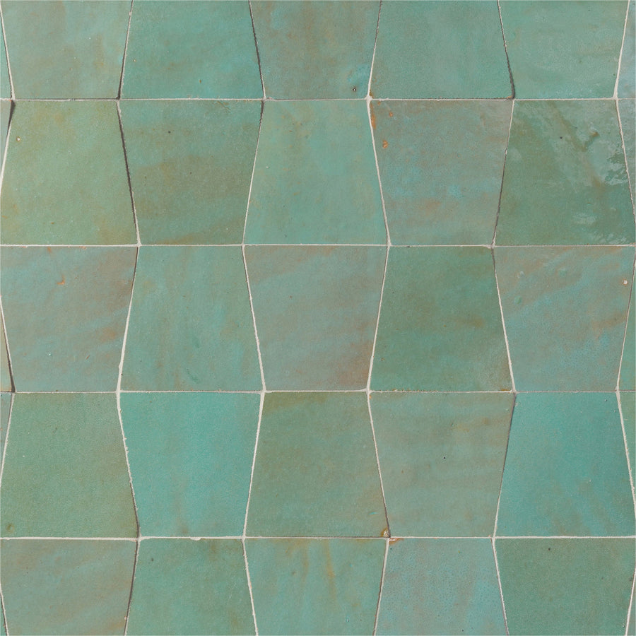 Close-up of Mistral Trapezoid 3x4 Tile in turquoise and teal, arranged in a staggered geometric pattern. Subtle color variations and white grout lines enhance the unique, handcrafted appeal of this elegant tile.