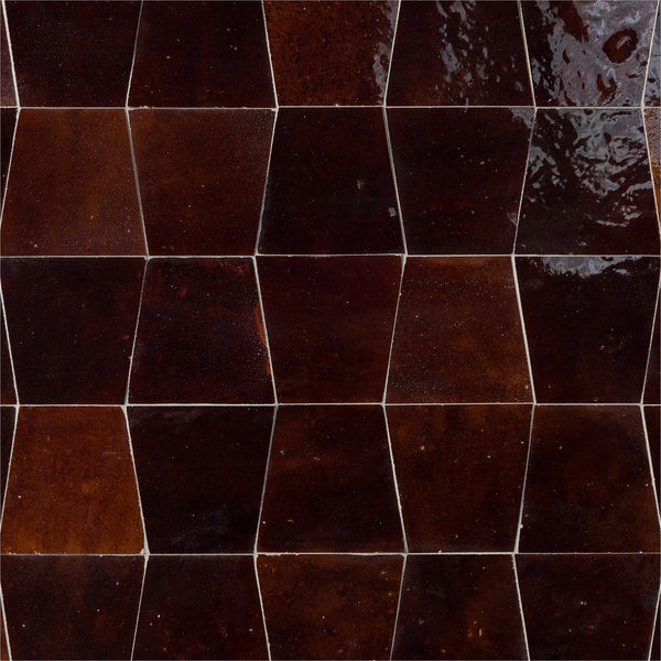 A close-up of a wall featuring glossy, dark brown Mistral Trapezoid 3x4 Tile arranged in a staggered geometric pattern. The elegant tiles have a slightly textured, reflective surface and visible grout lines.