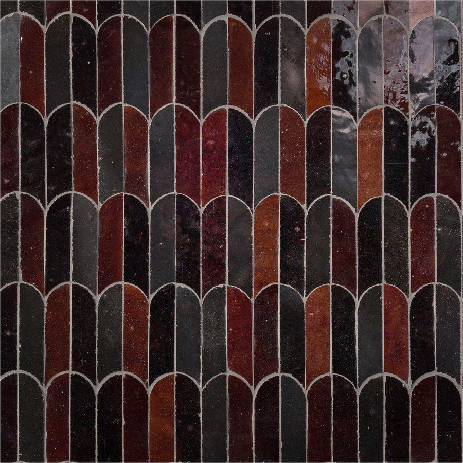 A close-up of the Mistral Bab Mosaic showcases its interlocking scallop pattern in dark brown, red, and black tones. Thin light grout lines and a glossy finish enhance the artistic elegance of this unique tile design.