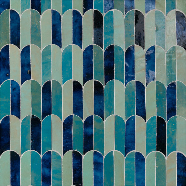 The Mistral Bab Mosaic features glossy, overlapping ceramic tiles in varied blue and green shades, arranged vertically to mimic fish scales or waves, creating an elegant artistic effect with light and dark tones.