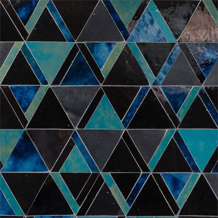 The Mistral Kilim Mosaic features a symmetrical geometric pattern of blue, green, and black glazed ceramic triangles, creating a sophisticated and visually striking tiled design.