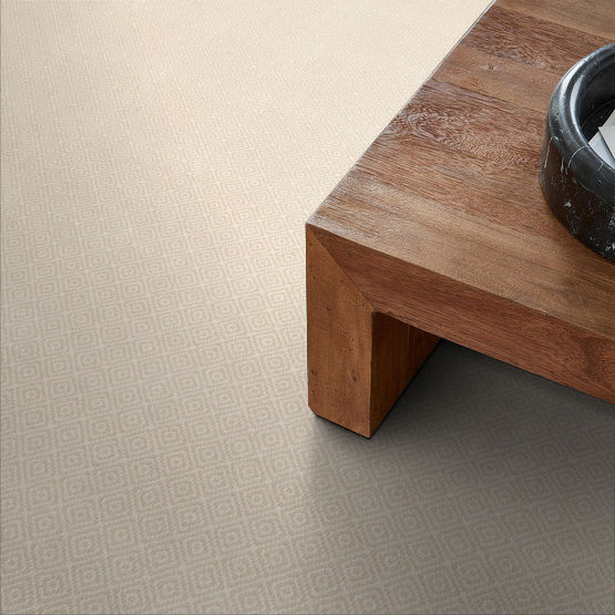 A close-up of a wooden table with a black decorative bowl on top, set on a beige carpet with a subtle geometric diamond pattern. The scene has a minimalist and modern aesthetic.