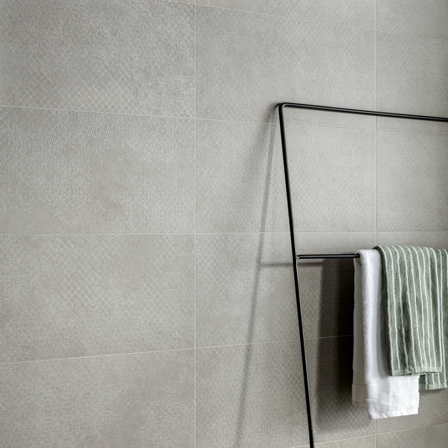 A minimalist metal towel rack holds a green and white striped towel and a white towel against a textured light gray tiled wall.