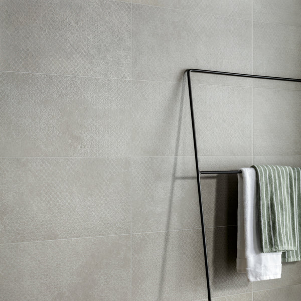 A minimalist metal towel rack holds a green and white striped towel and a white towel against a textured light gray tiled wall.