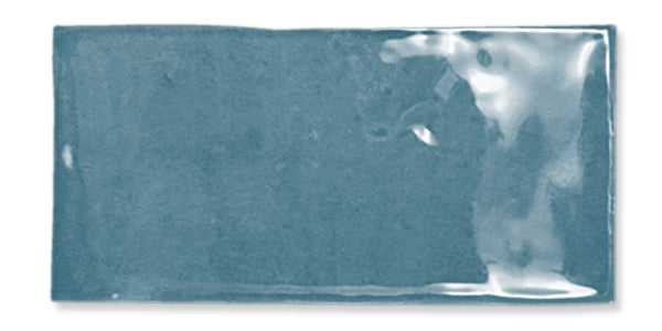 A rectangular blue ceramic tile with a glossy, reflective surface and slight color variations, displayed against a white background.