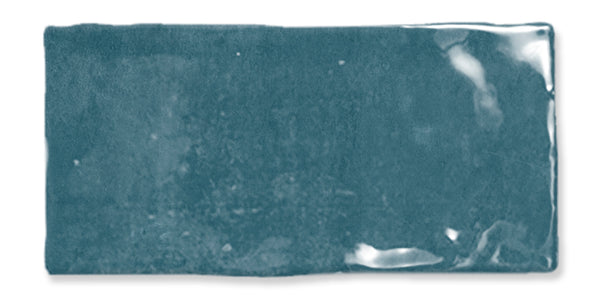 A rectangular, glossy teal ceramic tile with slightly uneven edges and a reflective surface, showing subtle variations in color and texture.
