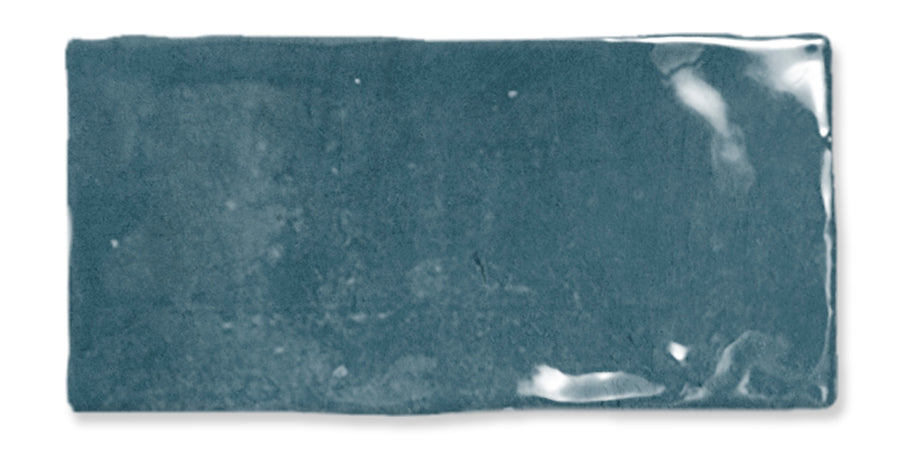 A rectangular, glossy teal ceramic tile with uneven edges and slight variations in the surface texture, reflecting light in a few spots.