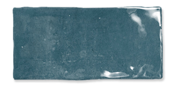 A rectangular, glossy teal ceramic tile with uneven edges and slight variations in the surface texture, reflecting light in a few spots.