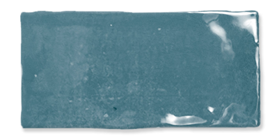 A rectangular teal ceramic tile with a glossy, reflective surface and slightly uneven edges, set against a white background.