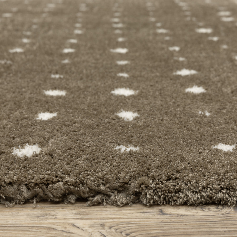 Close-up of a brown, shaggy rug with a soft texture, featuring small white polka dot patterns, placed on a light wooden floor.
