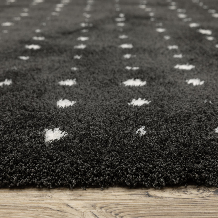Close-up of a dark gray, plush, textured rug with small white diamond patterns, placed on a light wood floor.