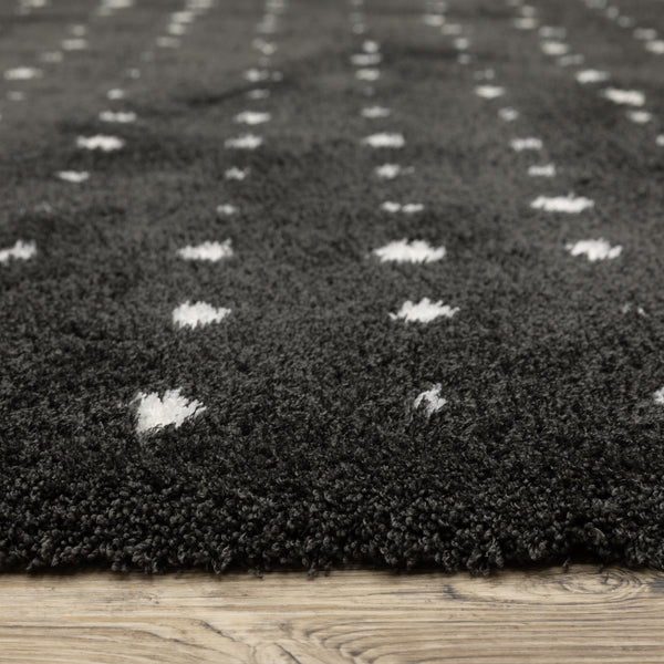 Close-up of a dark gray, plush, textured rug with small white diamond patterns, placed on a light wood floor.
