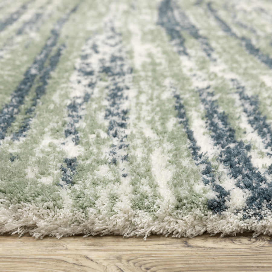 Close-up of a soft, shaggy area rug with a striped pattern in shades of green, blue, and white, placed on a light wooden floor.