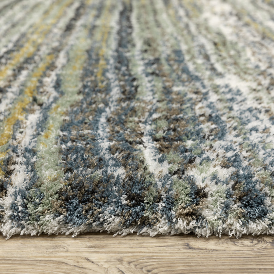 Close-up view of a plush, multicolored shag rug with blue, green, yellow, brown, and white fibers, resting on a light wood floor. The textured fibers create a soft and cozy appearance.