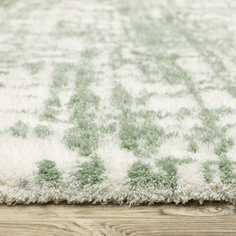 Close-up of a thick, plush rug with a white and light green pattern, resting on a wood floor. The texture of the rug fibers is clearly visible.