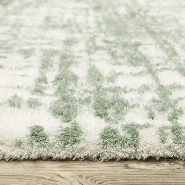 Close-up of a thick, plush rug with a white and light green pattern, resting on a wood floor. The texture of the rug fibers is clearly visible.