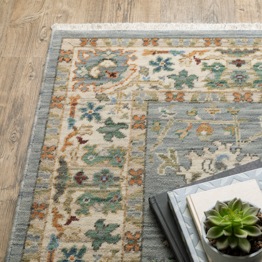 A close-up of a patterned area rug with muted green, blue, and orange designs on a wooden floor, next to stacked books and a small potted succulent.