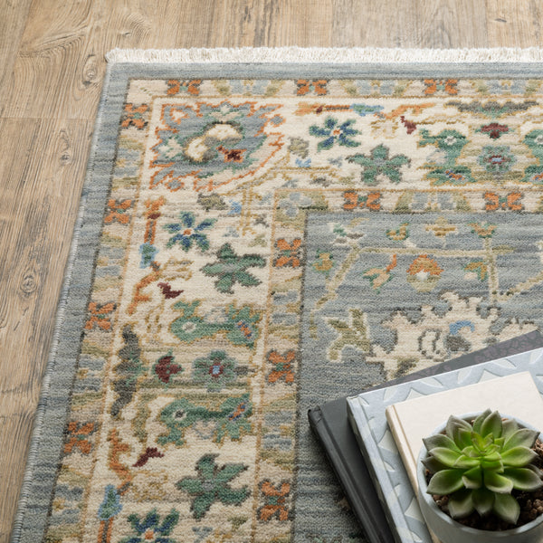 A close-up of a patterned area rug with muted green, blue, and orange designs on a wooden floor, next to stacked books and a small potted succulent.