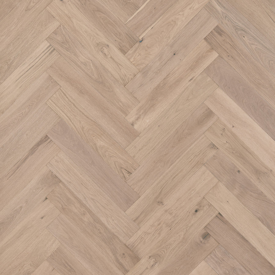 Main Street Herringbone White Oak Hardwood flooring features light brown planks in a classic herringbone pattern, highlighting visible wood grain and texture for an elegant, luxurious look.