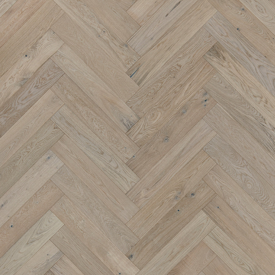 Main Street Herringbone White Oak Hardwood features light brown planks in a classic herringbone pattern, highlighting natural wood grain and small knots for a luxurious, textured, rustic look.