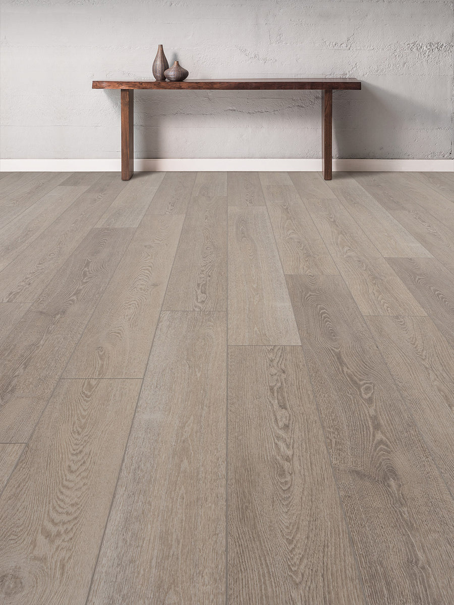 A minimalist room with Concorde 7.2" Luxury Vinyl Plank in light gray wood-look, a simple wooden bench against a plain wall, and three decorative vases neatly arranged on the bench.