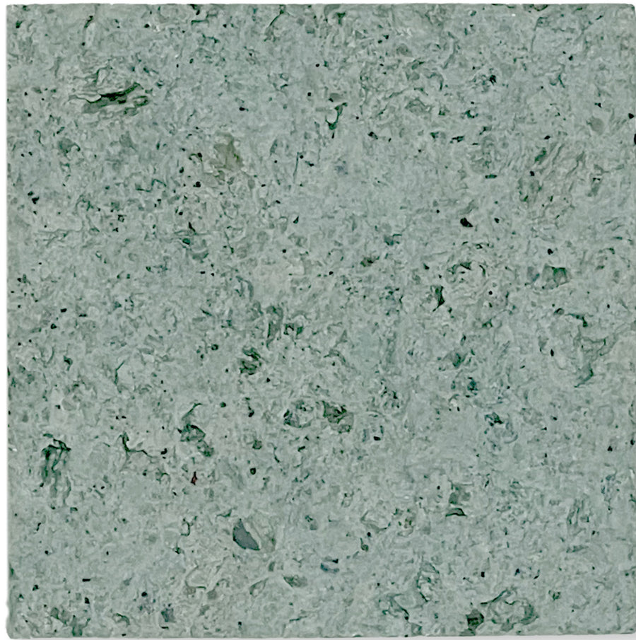 A close-up of Sukabumi Select 6x6 Honed Natural Stone reveals a textured gray-green surface with irregular patterns and dark and light flecks, mimicking premium material or natural stone.