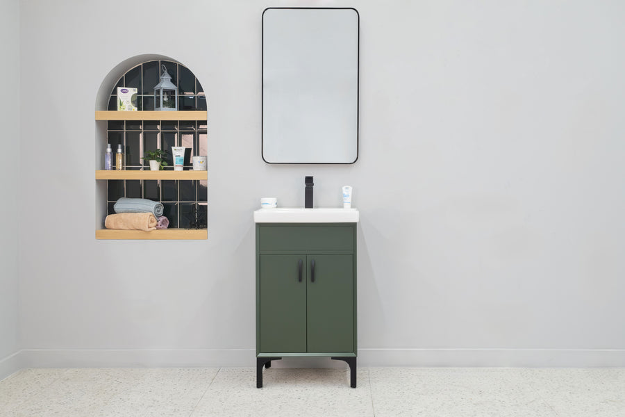 A minimalist bathroom showcases the Sempre 20" Vanity in green, topped with a white sink, paired with a rectangular mirror and an arched wall niche displaying toiletries and towels on shelves against a light gray wall.