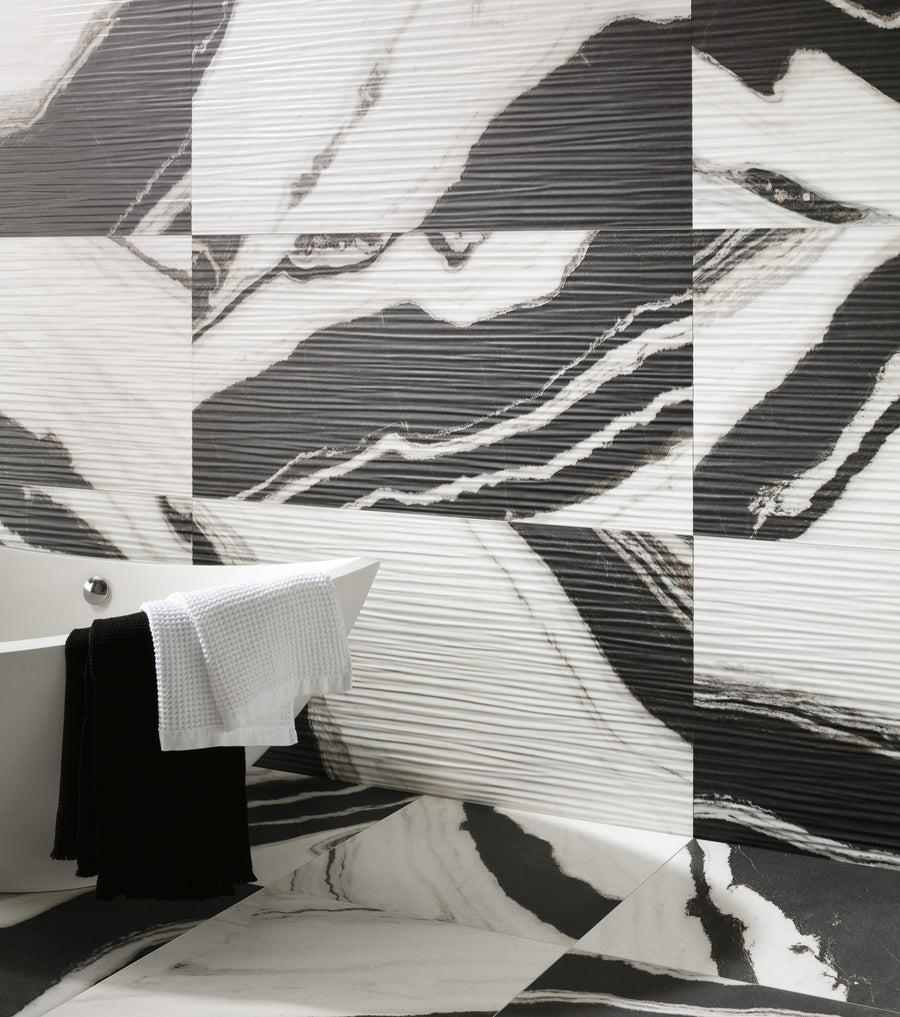 A modern bathroom features a white freestanding bathtub with a black and a white towel draped over the edge, set against large black-and-white marble-patterned tiles on the walls and floor.