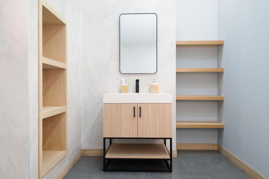 A modern bathroom with light wood shelves, a Solana 30" Vanity with white sink, black faucet, and a rectangular mirror. White and gray walls pair with dark gray tile flooring for a clean, contemporary vibe.