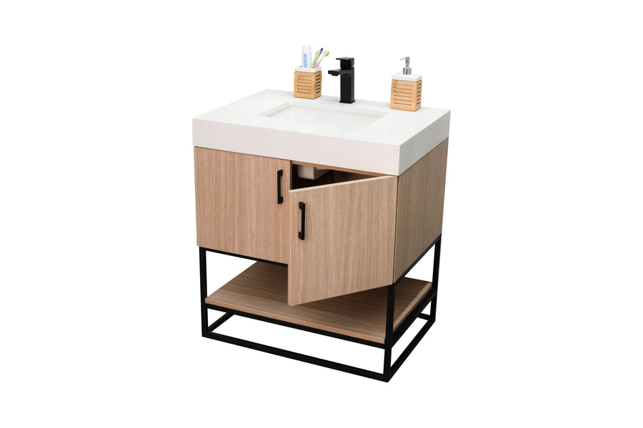 A modern bathroom vanity with a white sink, black faucet, light wood cabinet, black handles, open shelf at the bottom, and two containers holding toothbrushes and a soap dispenser.
