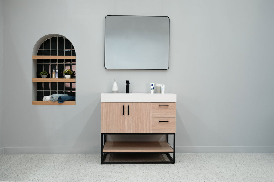 Minimalist bathroom with light gray walls features the Solana 36" Vanity topped by a rectangular mirror and neatly arranged toiletries. On the left, an arched wall shelf displays plants, towels, and decor.