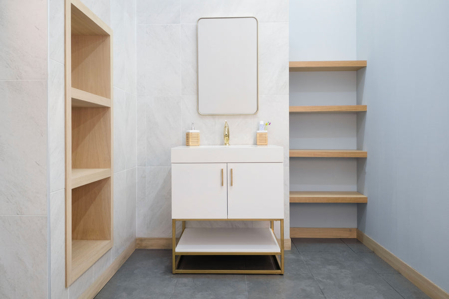 A modern bathroom features the Solana 30" Vanity, a gold faucet, and a rectangular mirror. Wooden shelves are on the right, built-in shelves on the left, all set against light walls and gray tile floors for a contemporary look.