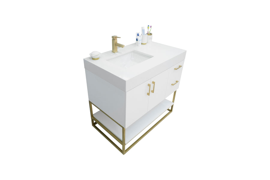 A modern white bathroom vanity with a rectangular sink, gold faucet, cabinet doors, drawers, and an open shelf below, set on a gold metal frame. Toiletries and a cup with toothbrushes are on top.