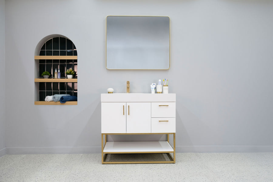 Modern bathroom with a Solana 36" Vanity featuring gold accents, a square mirror above, and a recessed shelf on the left displaying towels, toiletries, and small potted plants against a light gray wall.