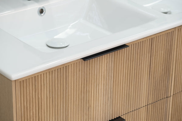 Close-up of a modern bathroom vanity with a white rectangular sink and a light wood cabinet featuring vertical grooves and a slim black handle.