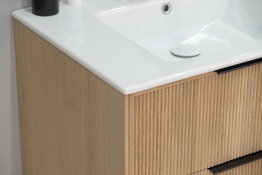 Close-up of a modern bathroom vanity with a white sink and a wooden cabinet featuring vertical grooves, black handles, and a minimalist design.