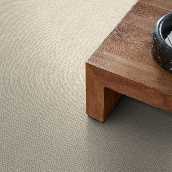 A close-up view of a wooden coffee table with a black bowl on top, placed on a beige carpet featuring a subtle diamond pattern.