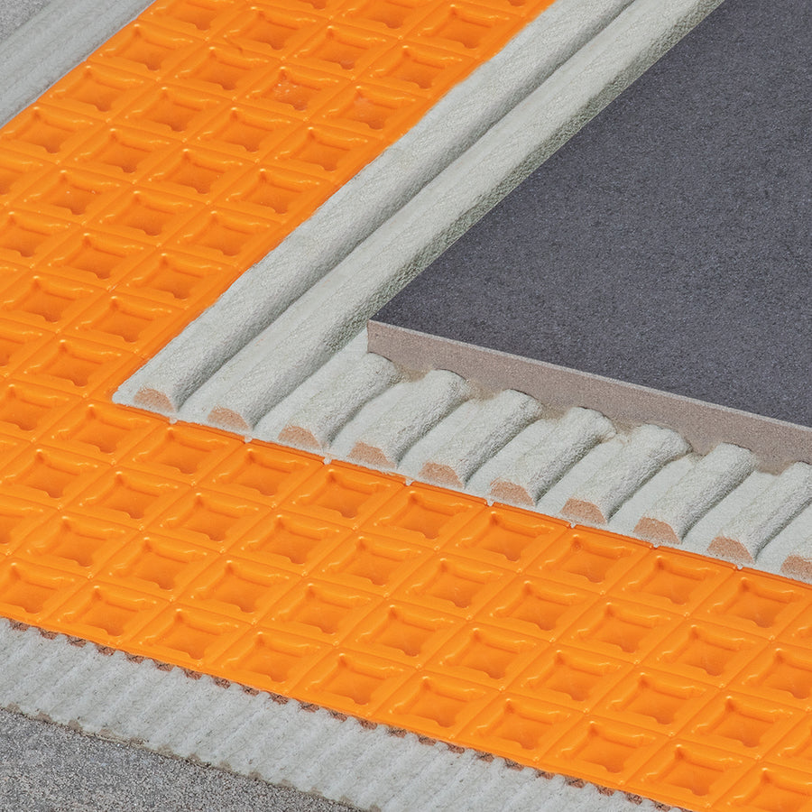 Close-up of a ceramic tile installation with gray tile, adhesive mortar, and an orange Schluter-Ditra Uncoupling Membrane with a grid pattern beneath, all layered on a flat surface.