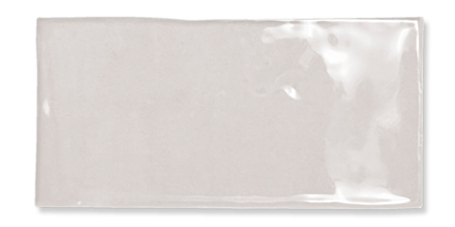 A single, rectangular, glossy light gray ceramic tile with a smooth surface and slightly uneven edges, positioned against a white background.