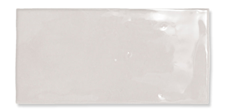 A rectangular, glossy, light gray ceramic tile with a smooth surface and slightly uneven edges, reflecting light in some areas.