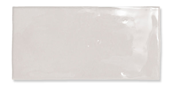 A rectangular, glossy, light gray ceramic tile with a smooth surface and slightly uneven edges, reflecting light in some areas.