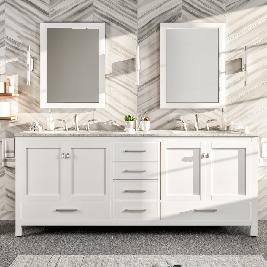 A modern bathroom showcases an Aberdeen 84" Double Bowl Vanity in white, two rectangular mirrors, and wall sconces. Gray and white chevron tiles accent the wall, while the countertop is adorned with small décor items and a plant.