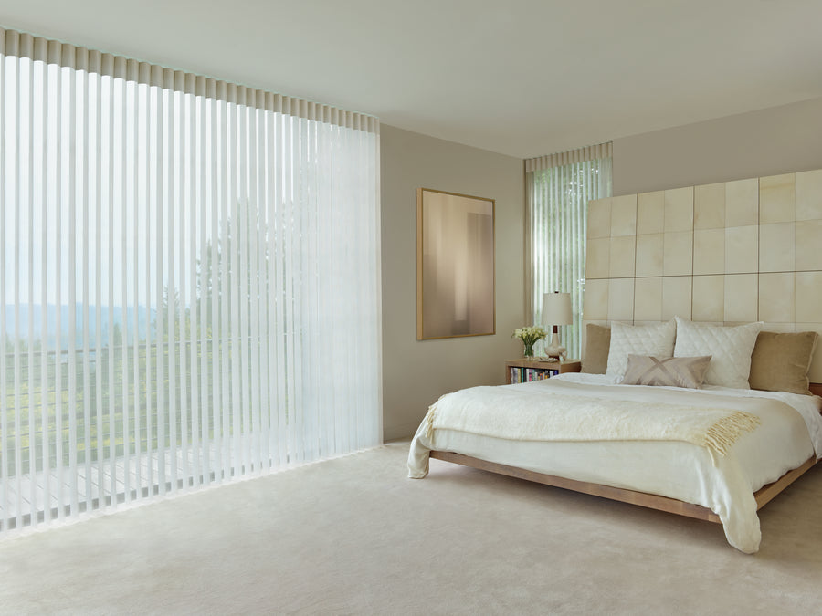 Modern bedroom with large floor-to-ceiling windows dressed in Luminette® Privacy Sheers, a beige upholstered headboard, neutral bedding, and minimalistic decor in soft, light tones.
