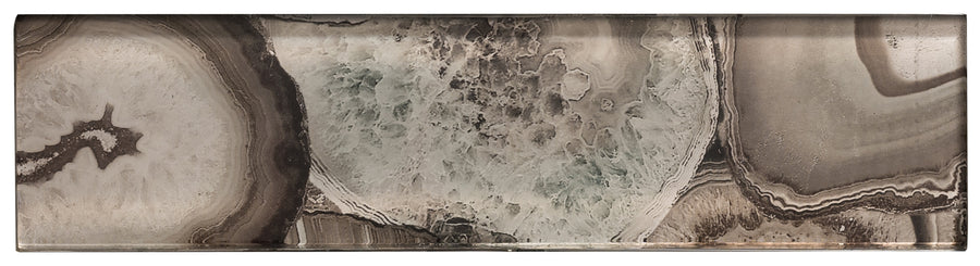 The Magical Forest 3x12 Glass Tile is a rectangular slab with layered agate patterns in brown, beige, and gray tones, featuring crystalline and banded textures that mimic the look of semi-precious stone.