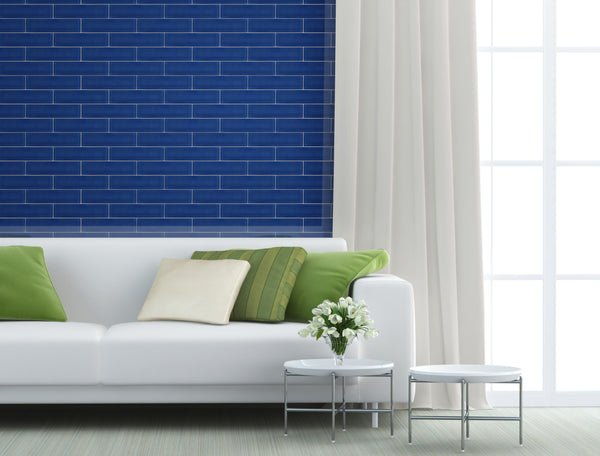 A modern living room with a white sofa, green and beige pillows, two round white tables with a small flower arrangement, Luna 3x12 Glass Subway Tile wall, and a large window with white curtains.
