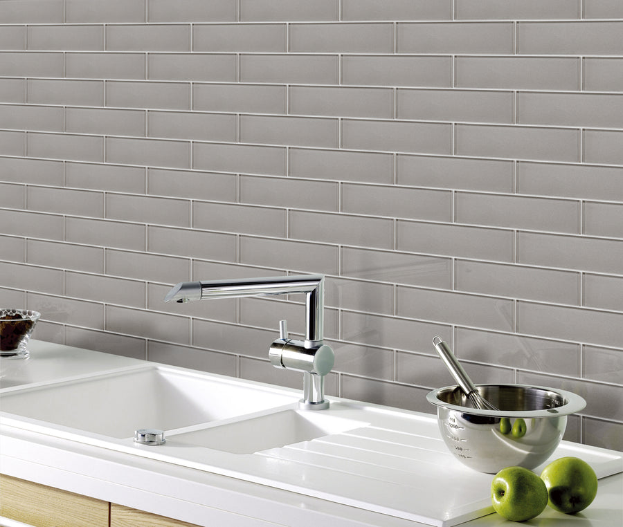 A modern kitchen countertop with a white sink, sleek chrome faucet, metal bowl, and green apples. The backsplash features Luna 3x12 Glass Subway Tile in a horizontal pattern for a fresh, contemporary look.