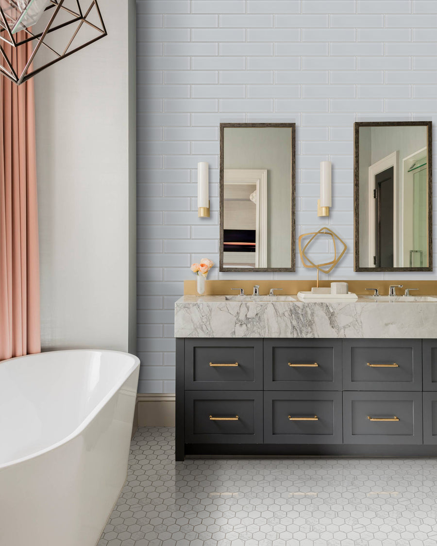 Modern bathroom featuring a freestanding white tub, double vanity with black drawers and gold handles, marble countertop, two mirrors, wall sconces, soft pink curtains, hexagonal floor tiles, and Luna 3x12 Glass Subway Tile on the walls.