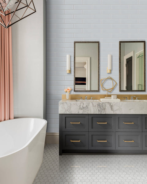 Modern bathroom featuring a freestanding white tub, double vanity with black drawers and gold handles, marble countertop, two mirrors, wall sconces, soft pink curtains, hexagonal floor tiles, and Luna 3x12 Glass Subway Tile on the walls.