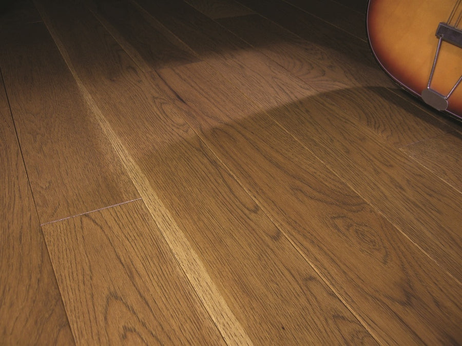 Close-up of Acadia 3 1/4" Hickory Hardwood floors, featuring a smooth brown finish. An acoustic guitar’s edge appears in the top right corner, casting a subtle shadow on the traditional hardwood surface.