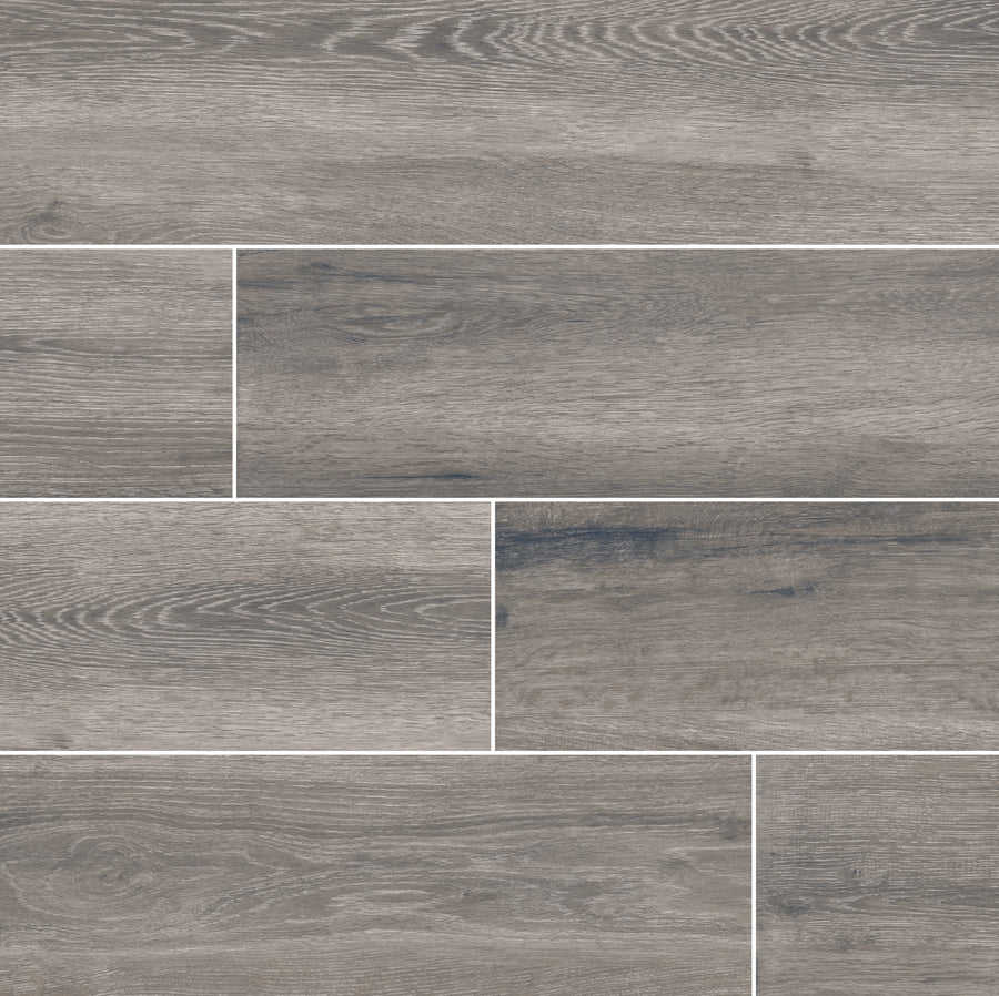 Antonius 6x36 Porcelain Tile in gray features a wood grain pattern and is arranged in a staggered layout, offering a modern and natural appearance reminiscent of wood look porcelain flooring.